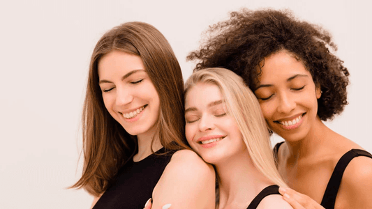 Three smiling women of diverse backgrounds enjoying natural skincare together.